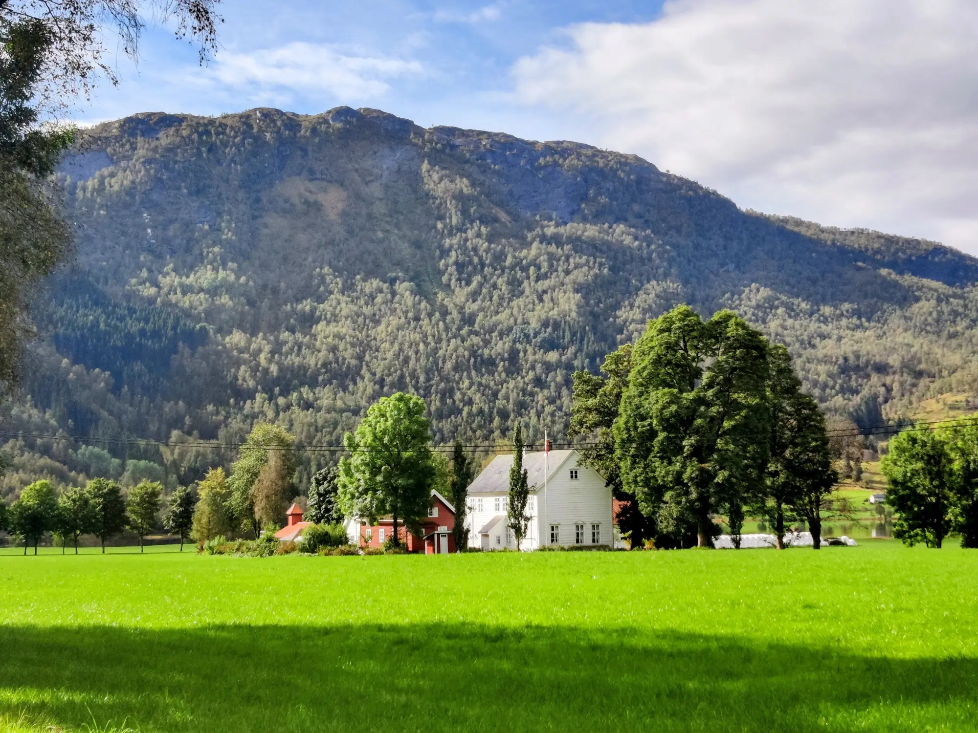 Osen Gard, eit flott kvit gardsbygg i vestnorsk herregard stil står fram over grønnt gras, træer og høge fjell.